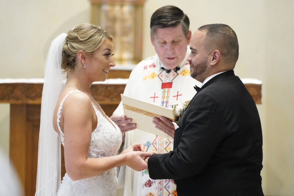 Christina MacDougall places a wedding band on Julio Prendergast's finger as Msgr. Francis J. Schneider officiates their wedding Mass Aug. 20, 2021, at St. John the Baptist Church in Wading River, N.Y.