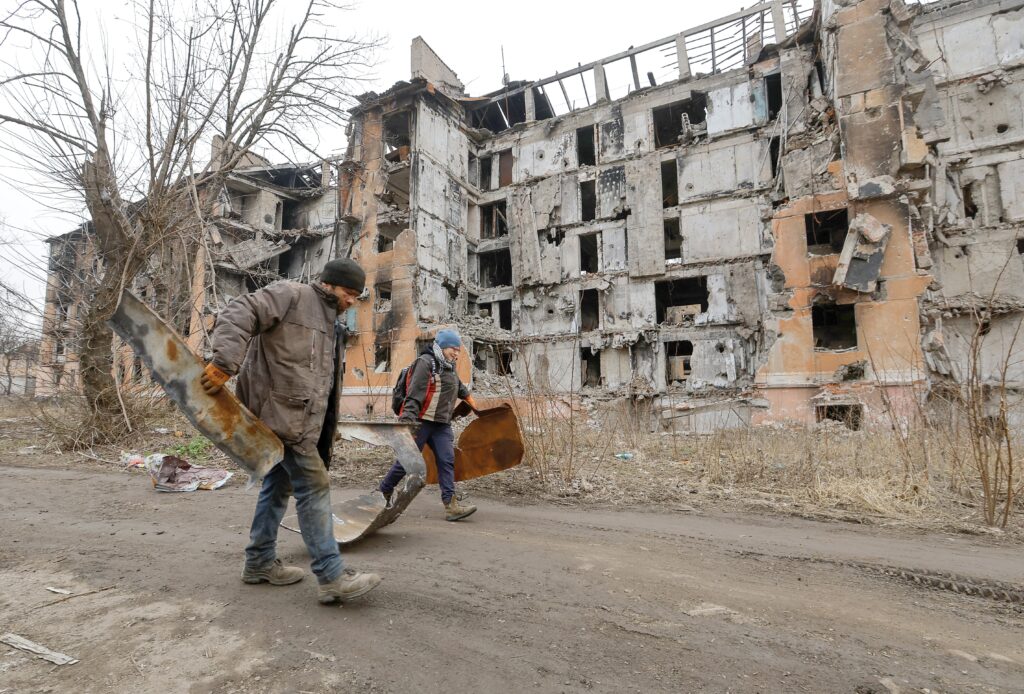 Local residents walk past a multistory apartment block in Mariupol, Ukraine, March 16, 2023, which was destroyed during the Russian invasion.