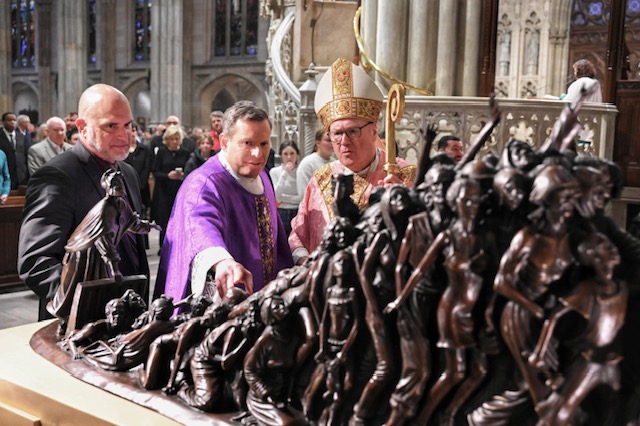 Sculptor Timothy Schmalz (left), Father Enrique Salvo, rector of St. Patrick's Cathedral (center), and Cardinal Timothy Dolan (right) look at the new human trafficking statue installed at St. Patrick's Cathedral, March 17, 2023.