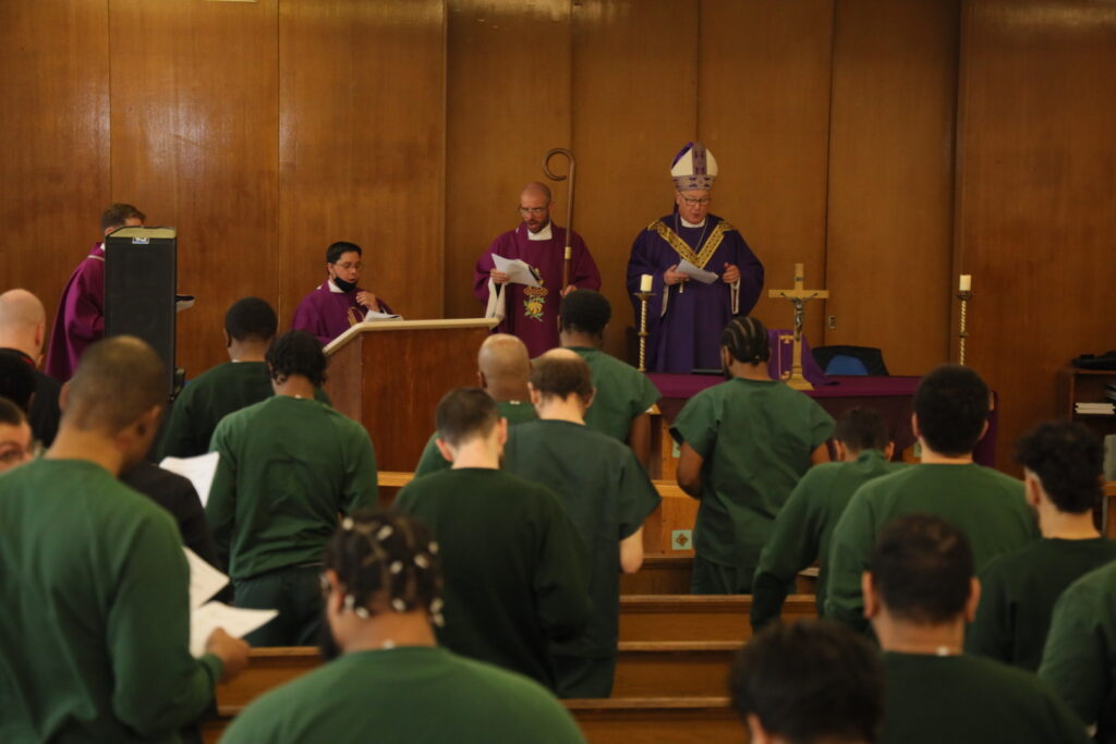 Cardinal Timothy Dolan (standing, right) delivers a homily to staff and detainees at the Eric M. Taylor Center on Rikers Island, April 5, 2023.