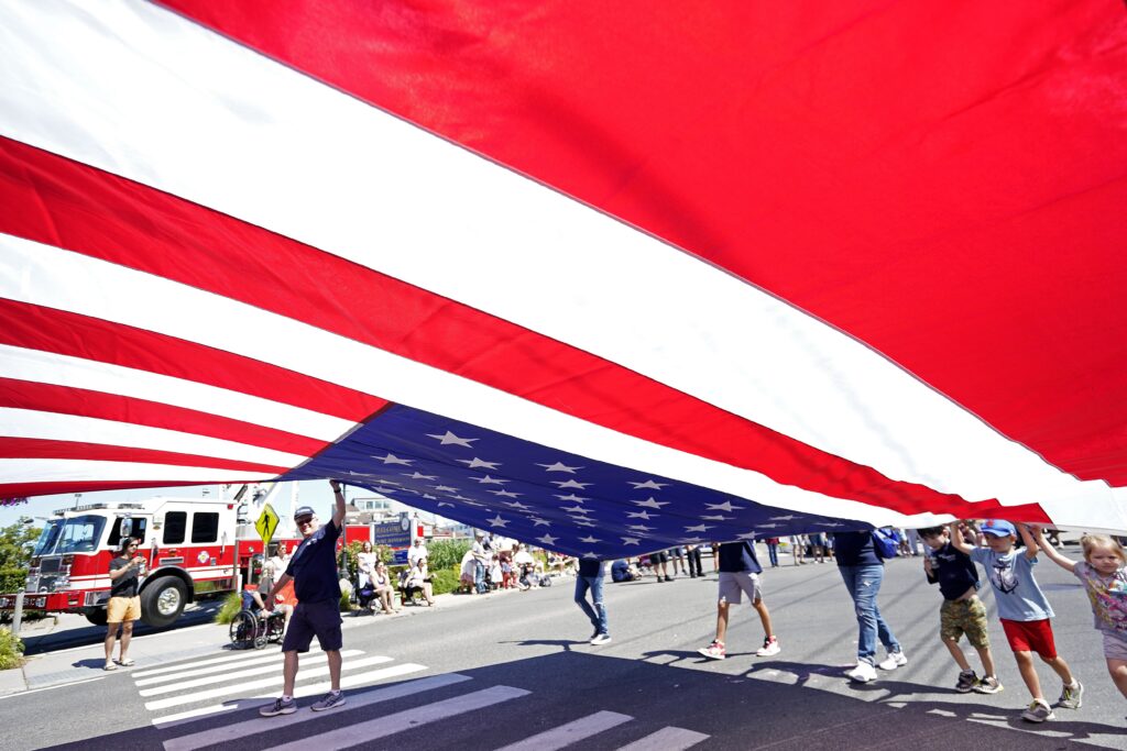 Marchers grip a giant U.S. flag as they participate in the Independence Day parade in Port Jefferson, N.Y., July 4, 2022.