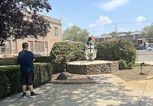 An onlooker stands near a statue of Mary that was vandalized July 8 at Resurrection Church in Gerritsen Beach in the Diocese of Brooklyn.