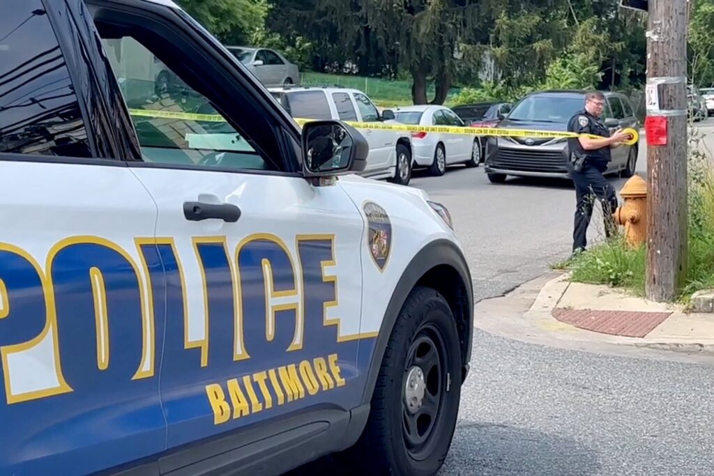 A police officer, seen in a still image from video, secures crime scene tape to a pole July 2, 2023, after a mass shooting at the scene of a Fourth of July holiday weekend block party in Baltimore.