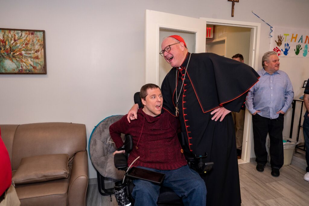 Cardinal Timothy Dolan (center, standing) shares a laugh with a resident of ArchCare at St. Teresa in Staten Island, May 10, 2023.