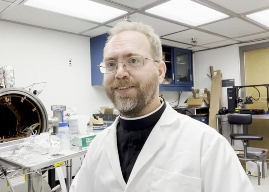 Jesuit Brother Robert Macke presents a device to study the porosity and density of specimens retrieved from the asteroid Bennu by the Osiris-Rex space mission at the Lunar and Planetary Laboratory in Tucson as seen in a YouTube video he posted on his channel Aug 12, 2022.