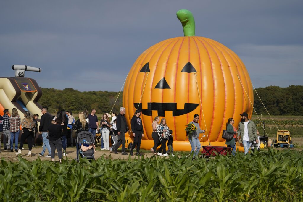 People walk past an inflatable pumpkin as they attend a fall festival in Manorville, N.Y., Oct. 16, 2022.