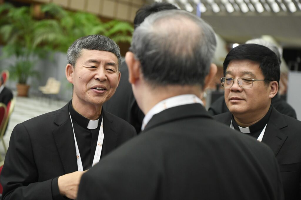 The two members of the assembly of the Synod of Bishops from mainland China, Bishops Anthony Yao Shun of Jining and Joseph Yang Yongqiang of Zhoucun, speak with other participants before work begins Oct. 14, 2023, in the Paul VI Audience Hall at the Vatican.