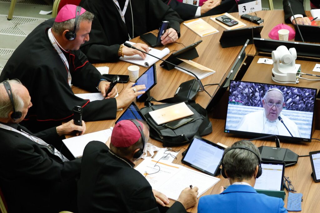 Participants watch Pope Francis on a video screen as they work on their tablets with synod documents during the first session of the assembly of the Synod of Bishops in the Paul VI Audience Hall at the Vatican on October 4, 2023.