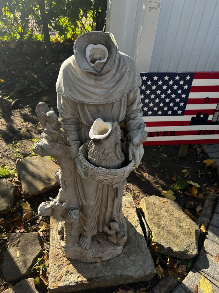 The desecrated statue of Saint Francis stands in the 9/11 remembrance garden of Sacred Heart Church in Staten Island. The statue was found decapitated on November 2, 2023. The missing piece has been located and repairs are underway.