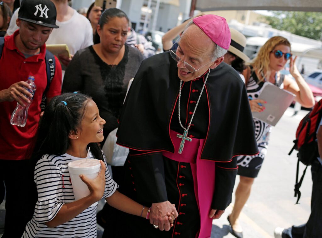 Bishop Mark J. Seitz of El Paso, Texas, shares a smile with a Honduran girl named Cesia as he walks and prays with a group of migrants at the Lerdo International Bridge in El Paso on June 27, 2019.