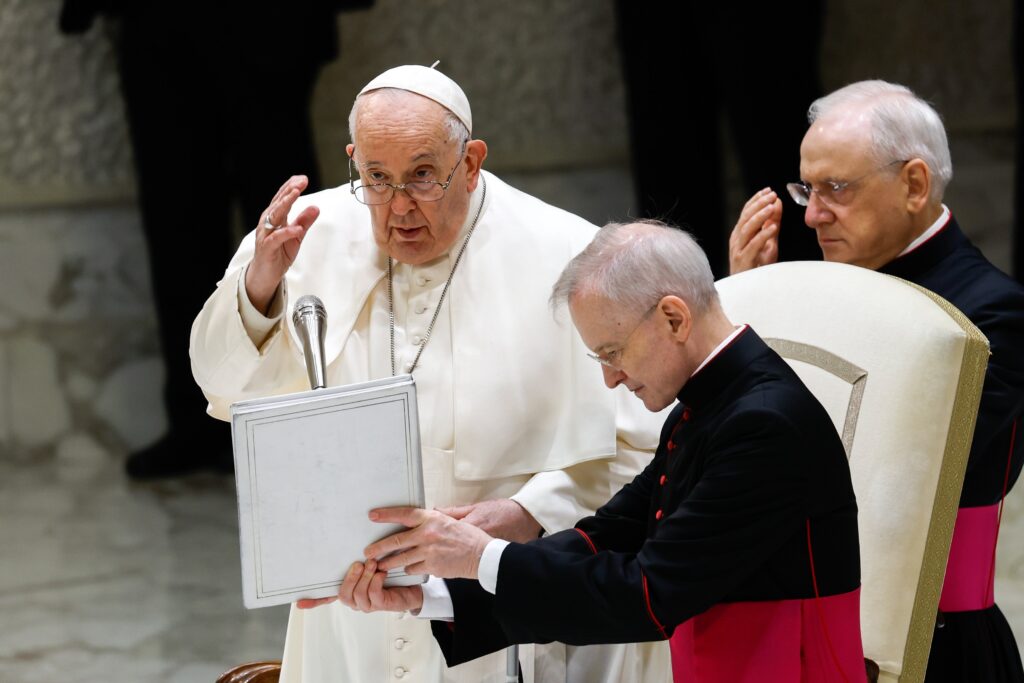 Pope Francis gives his blessing at the end of his weekly general audience as Monsignor Luis Maria Rodrigo Ewart, an aide, holds the pope's prayer book in the Paul VI Audience Hall at the Vatican on December 20, 2023.