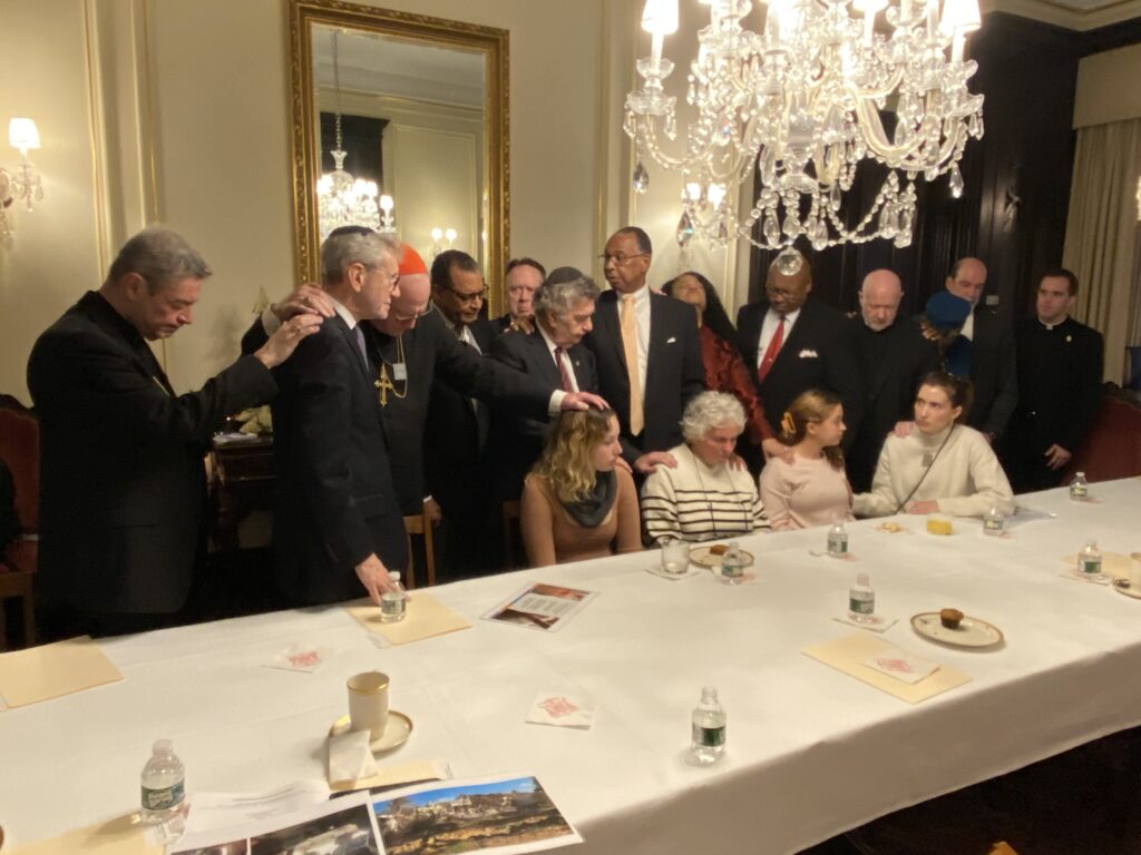 Cardinal Timothy Dolan (third left, with red zucchetto), and other New York faith leaders participate in a laying-on of hands at the conclusion of a meeting with survivors of the October 7 attacks in Israel and representatives of the Jewish Agency for Israel (seated).