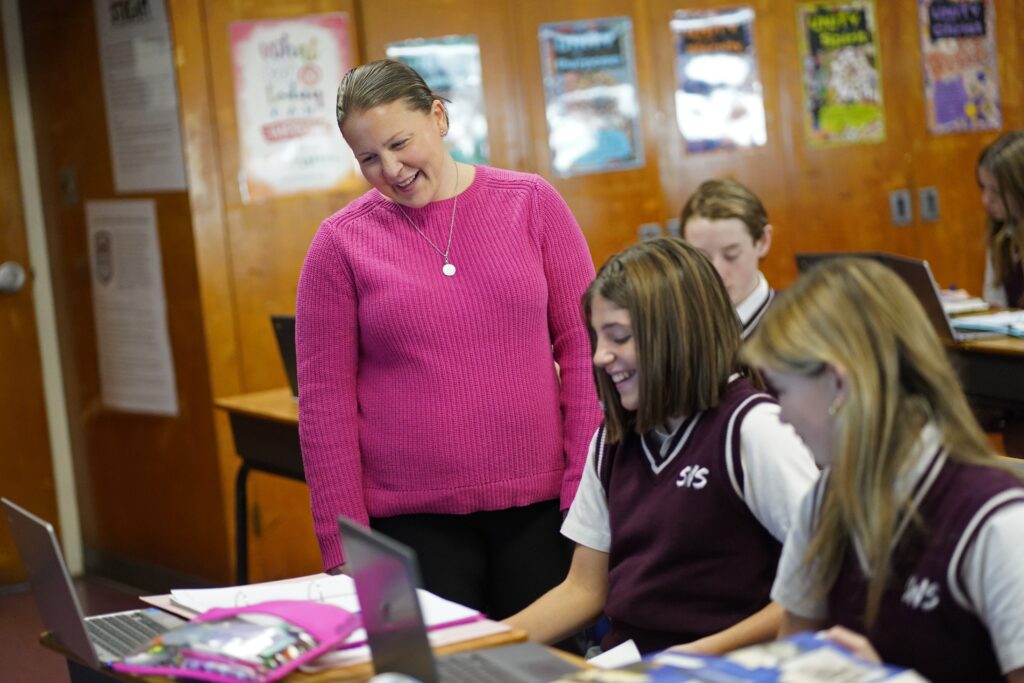 Social studies teacher Mary Bradley smiles as she reviews student assignments during an eighth-grade class at St. William the Abbot School in Seaford on December 13, 2023.
