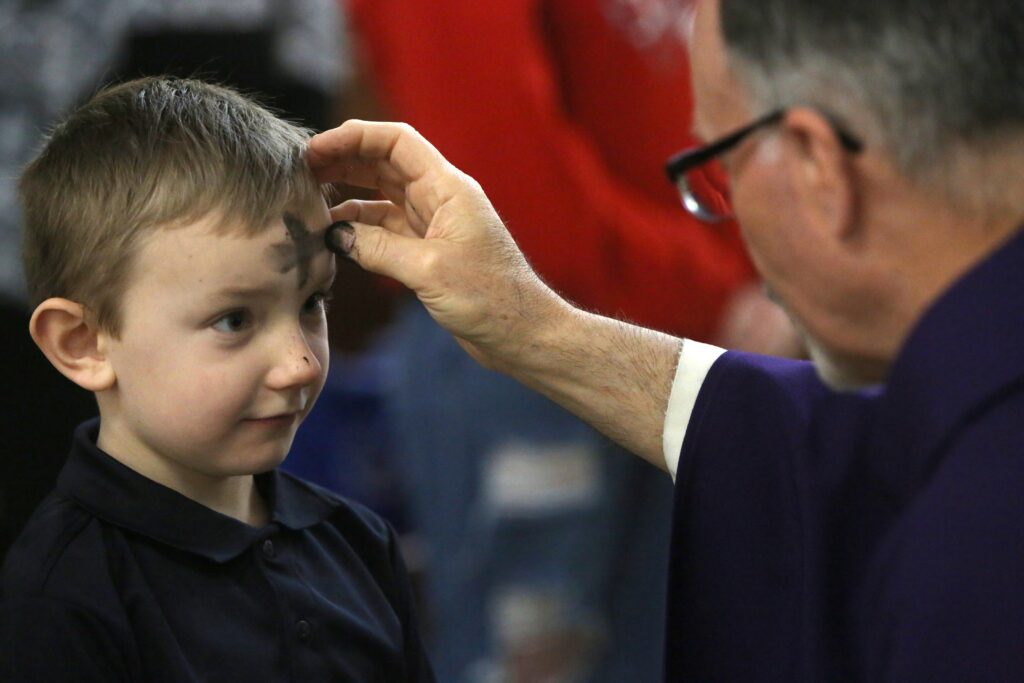 Father John Dakes, pastor of Jesus the Divine Word Church in Huntingtown, Maryland, places ashes on a child's forehead during Ash Wednesday Mass on February 22, 2023.