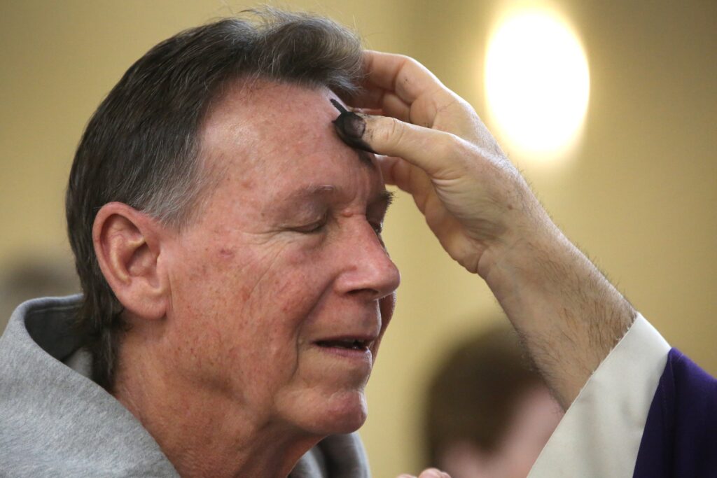 Father John Dakes, pastor of Jesus the Divine Word Church in Huntingtown, Maryland, places ashes on a man's forehead during Ash Wednesday Mass on February 22, 2023.