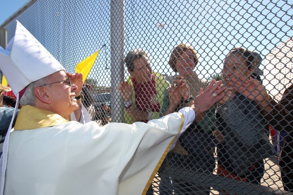 Bishop Mark J. Seitz of El Paso, Texas, touches the hands of people in Mexico through a border fence following Mass in Sunland Park, New Mexico, in this 2014 file photo.
