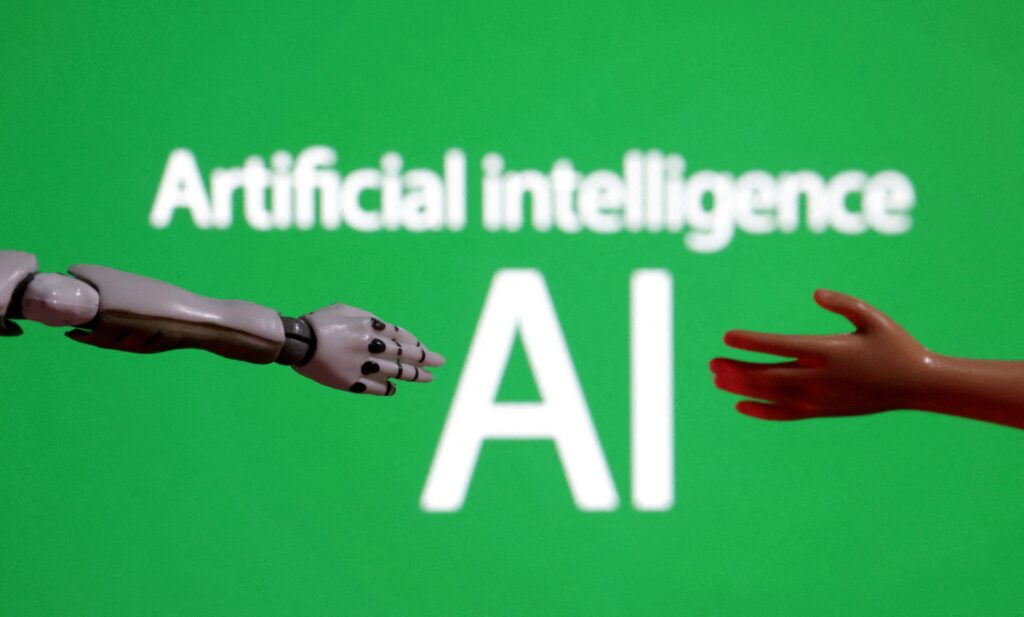 The words "Artificial intelligence AI" are pictured with a miniature of a robot arm and a toy hand in this December 14, 2023, illustration.