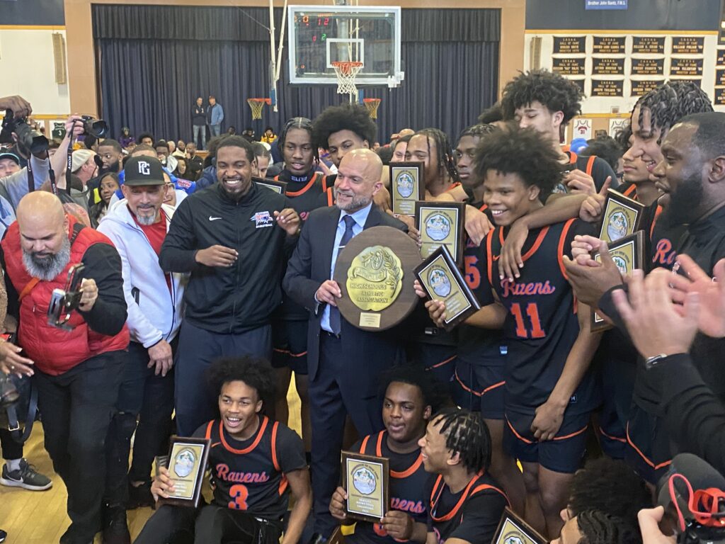 St. Raymond's School for Boys Coach Jorge Lopez (center, with trophy) celebrates with his staff and players after they defeated Archbishop Stepinac High School to win the CHSAA "AA" boys' basketball championships, February 25, 2024.