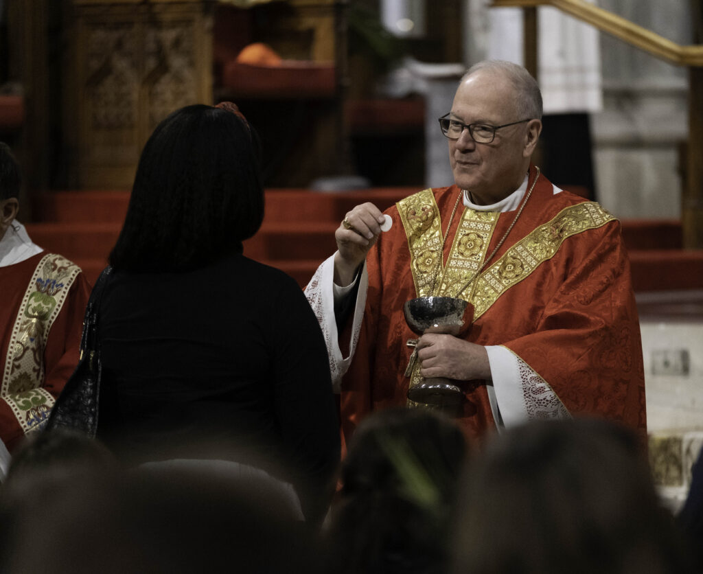 Cardinal Timothy Dolan (right) distributes communion during Palm Sunday Mass at St. Patrick's Cathedral in Manhattan, March 24, 2024.