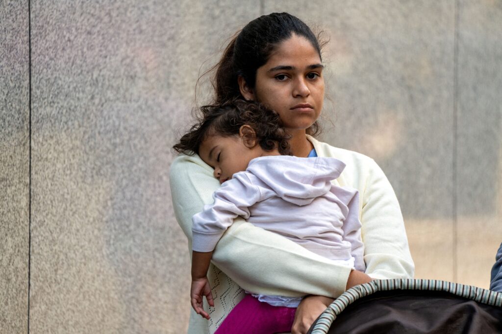 A migrant and her daughter wait for aid outside the offices of Catholic Charities in New York City Aug. 16, 2022, after being transported via charter bus from Texas.