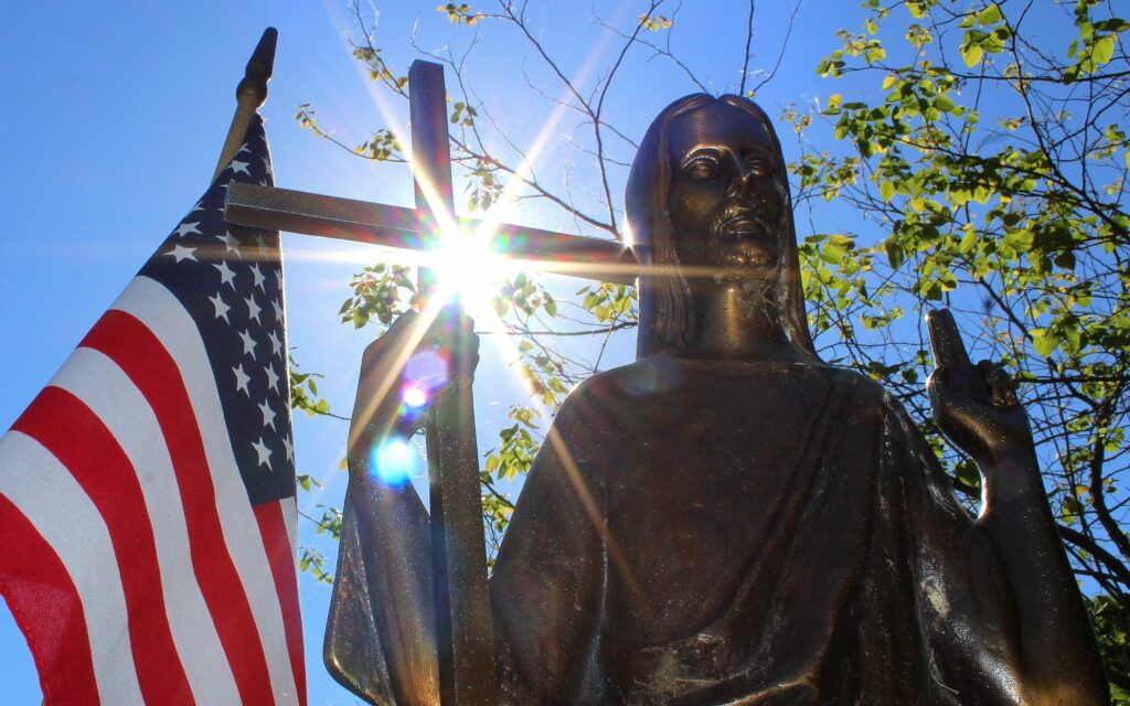 Sun shines through a statue of Christ on a grave marker alongside an American flag at St. Mary Catholic Cemetery in Appleton, Wisconsin in this 2018 photo.