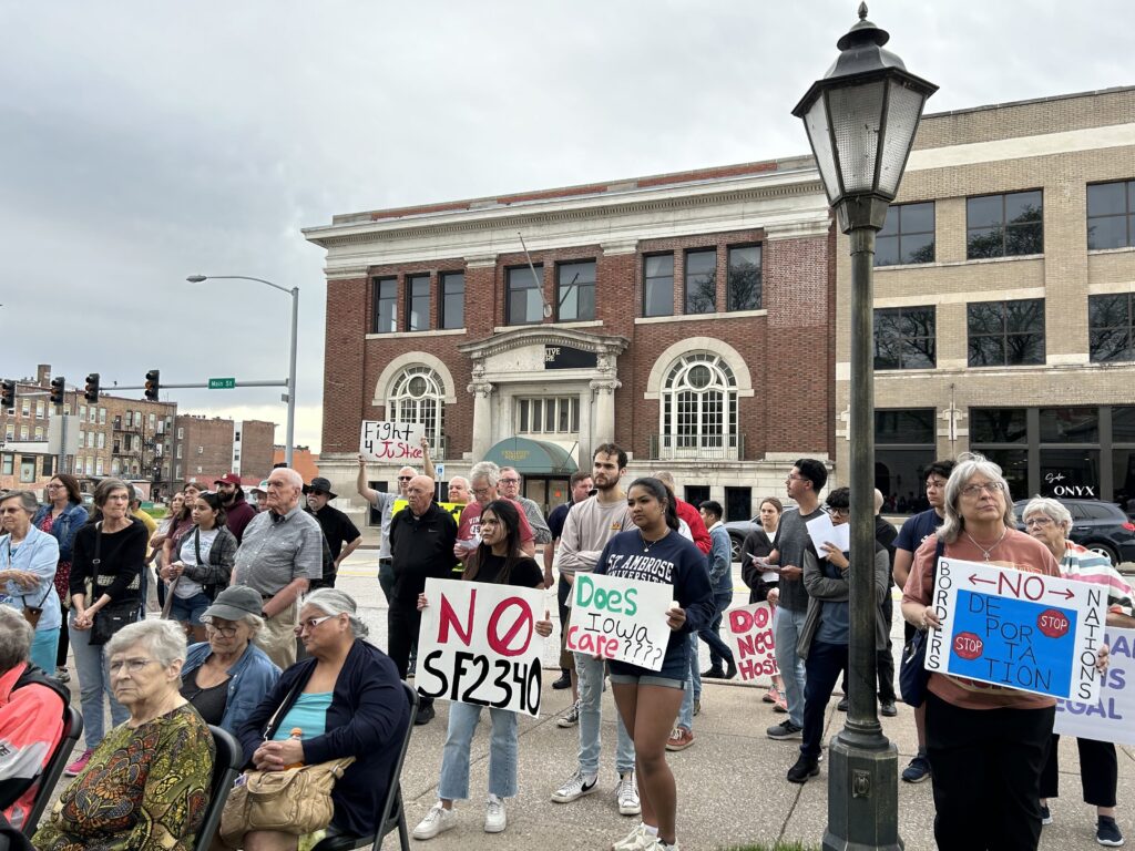 Participants at the "For Human Dignity" vigil/rally outside St. Anthony Catholic Church in Davenport, Iowa, May 1, 2024, hold placards protesting Iowa's new law that makes it a state crime for illegal reentry into Iowa.