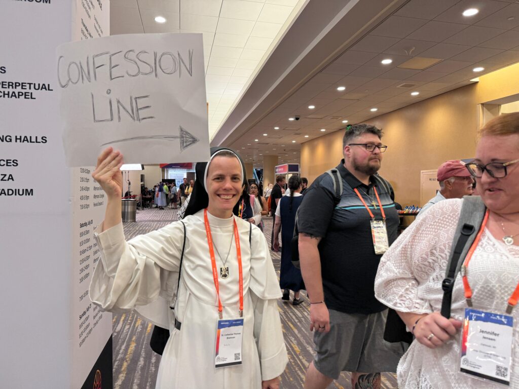 Sister Catherine Thomas Brennan holds a sign guiding participants of the National Eucharistic Congress to the confession line, July 19, 2024.