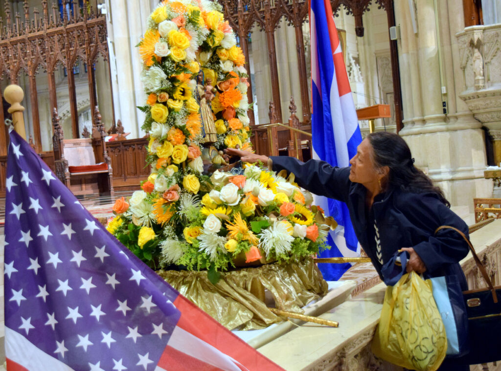 A woman places a flower next to a statue of La Virgen de la Caridad del Cobre in 2018.