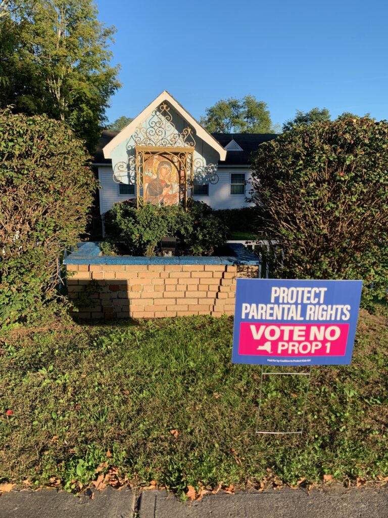 A sign urging a NO vote on Proposal One flanks an icon of the Blessed Virgin Mary with the Baby Jesus on the grounds of Sacred Heart Church, Esopus.