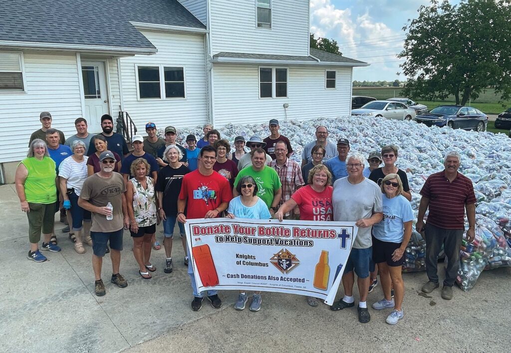 Members of the Knights of Columbus and family members from Monsignor Esper Council 3027 in Fowler, Michigan, gather near 131,000 bottles and cans collected during the council’s annual Returns for Vocations fundraiser.