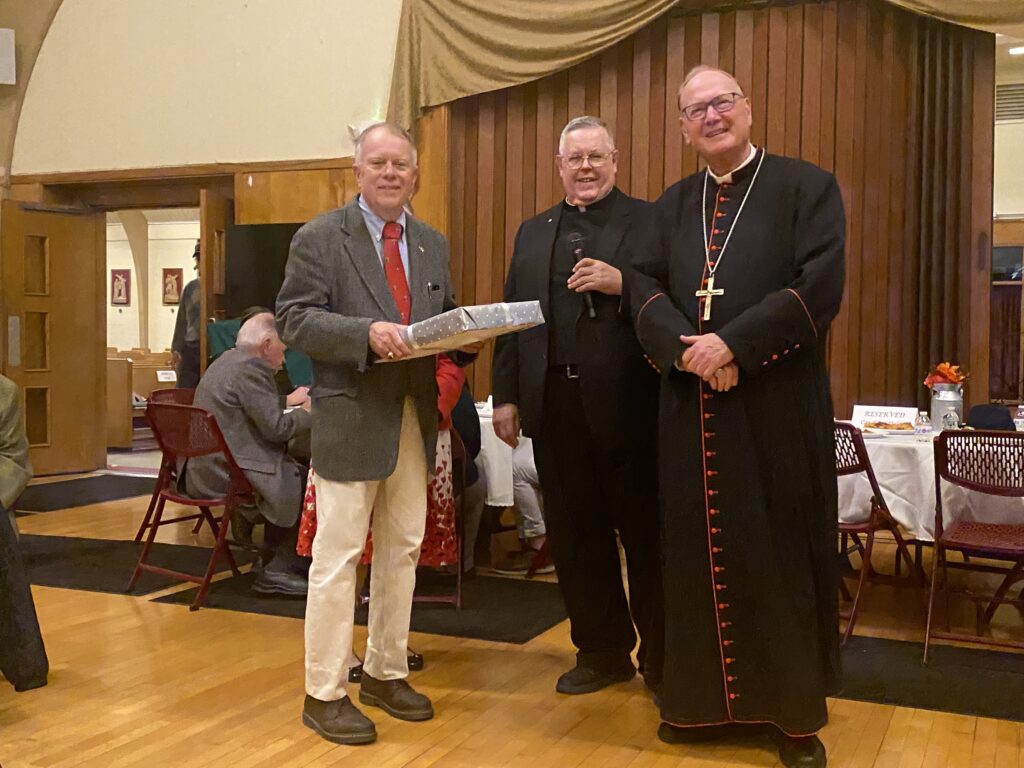 James Patrick Donick (left), newly installed as a lay acolyte, offers a gift to Cardinal Timothy Dolan (right) as St. Stanislaus Kostka parish pastor Father Karl A. Lindblad (center) looks on, November 9, 2024.