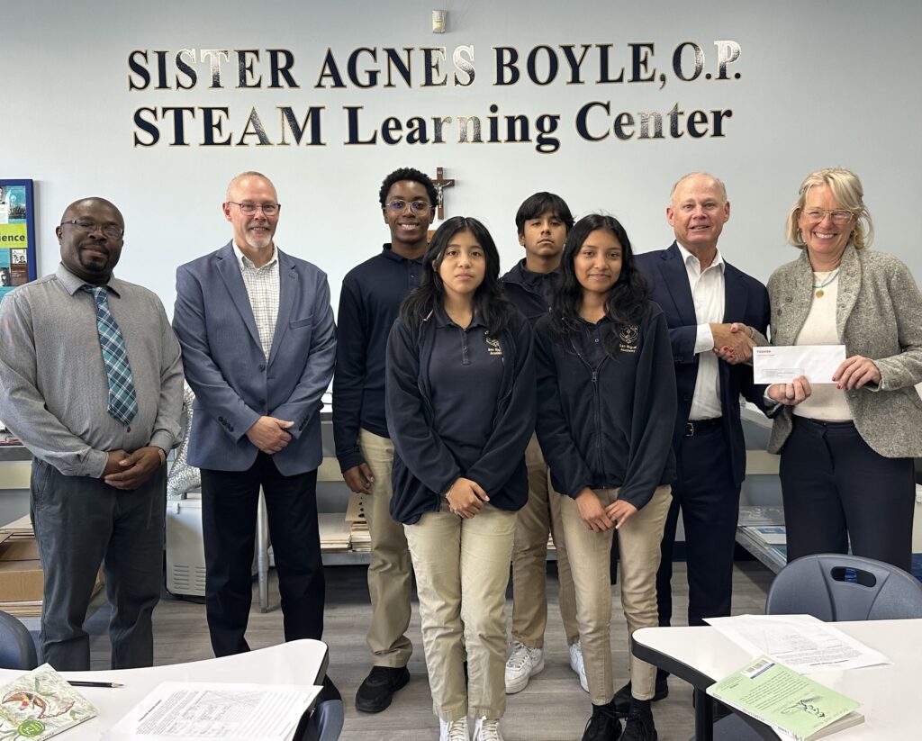 Senior Account Executive Karl Robisch and Executive Vice President Tom Becker present the Toshiba grant award to San Miguel Academy science teacher Effiong Eyo (far left) and Director of Curriculum Molly Albrecht (far right) along with four of the eighth-grade students who will be participating in the project.