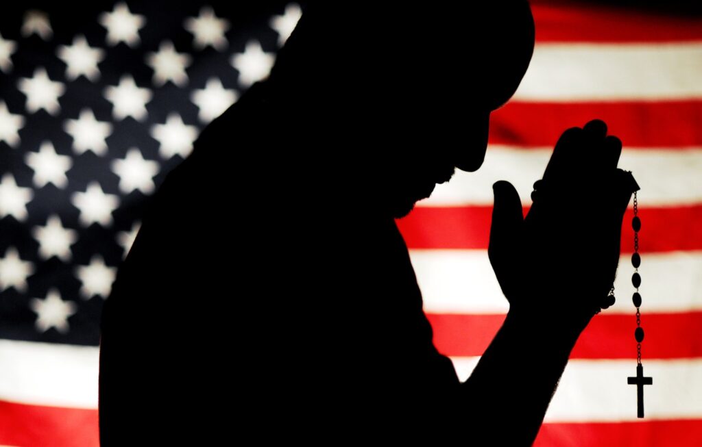 A man holding a rosary with the U.S. flag as a backdrop is silhouetted in this photo illustration. (OSV News file illustration/Mike Crupi, Catholic Courier)