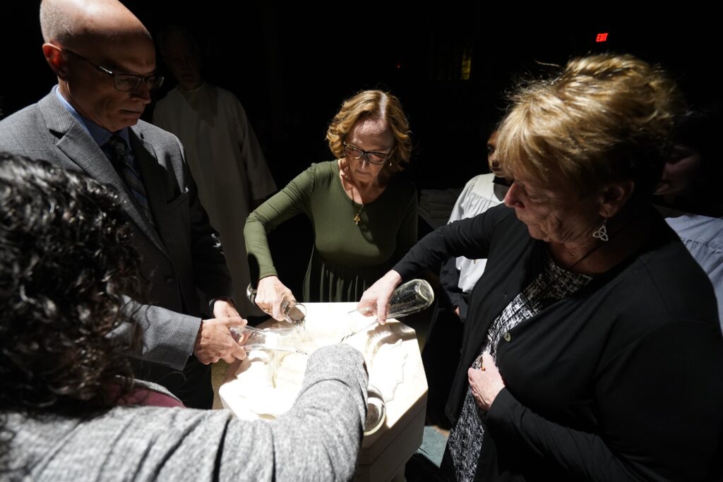 Leaders of the parish faith formation ministry pour water into the baptismal font during the Easter Vigil at St. John the Evangelist Church in Center Moriches, April 8, 2023.