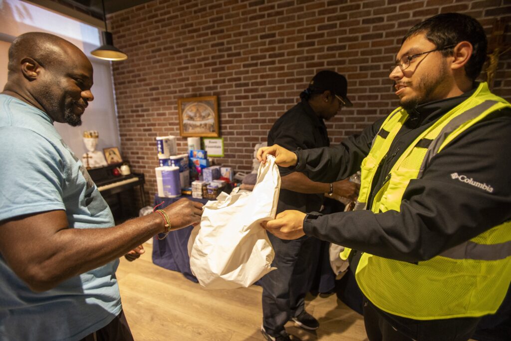 Volunteer Abel Garcia, right, helps distribute essential daily items to a man displaced by wildfires at the "Eaton Fire Parish Response" at St. Philip the Apostle Church in Pasadena, Calif., January 10, 2025.