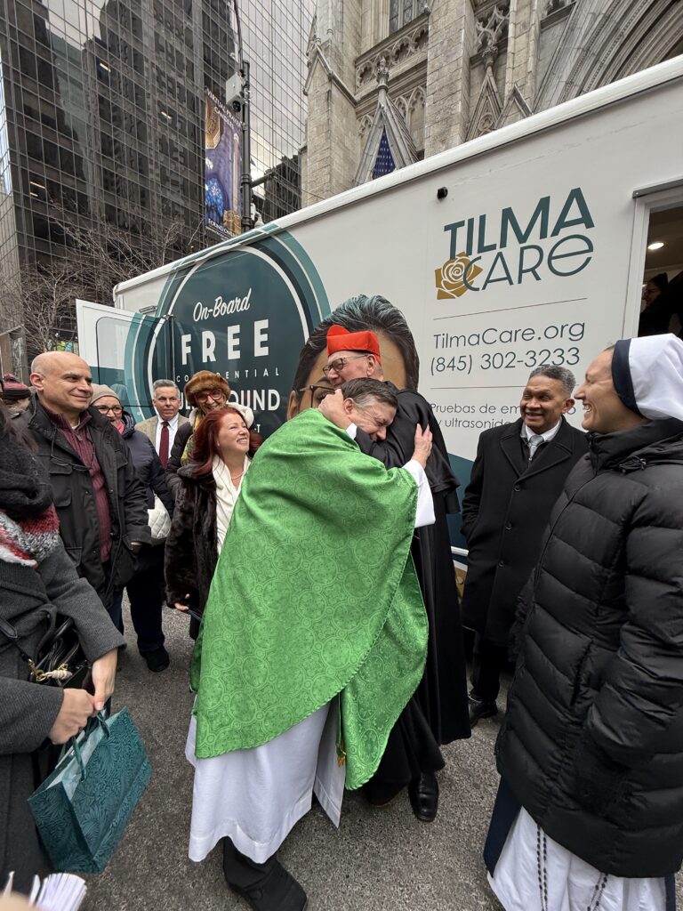 Cardinal Timothy Dolan (in black) embraces Father Richard Gill, pastor of St. Lawrence O’Toole and Sacred Heart Parishes in Brewster, at the blessing of their mobile ultrasound van in front of St. Patrick’s Cathedral, Sunday, January 26, 2025. Siobhan Fitzpatrick (center left), whose family made a significant donation to the van’s purchase, looks on.