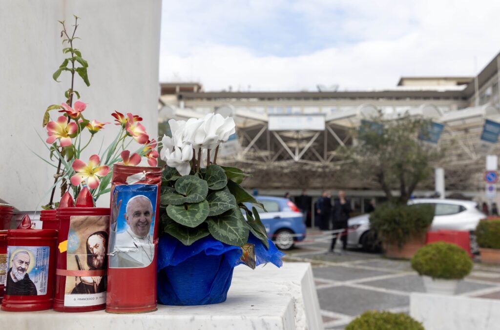 Flores y velas votivas en la base de una estatua de San Juan Pablo II frente al hospital Gemelli de Roma el 18 de febrero de 2025, donde el Papa Francisco está hospitalizado.