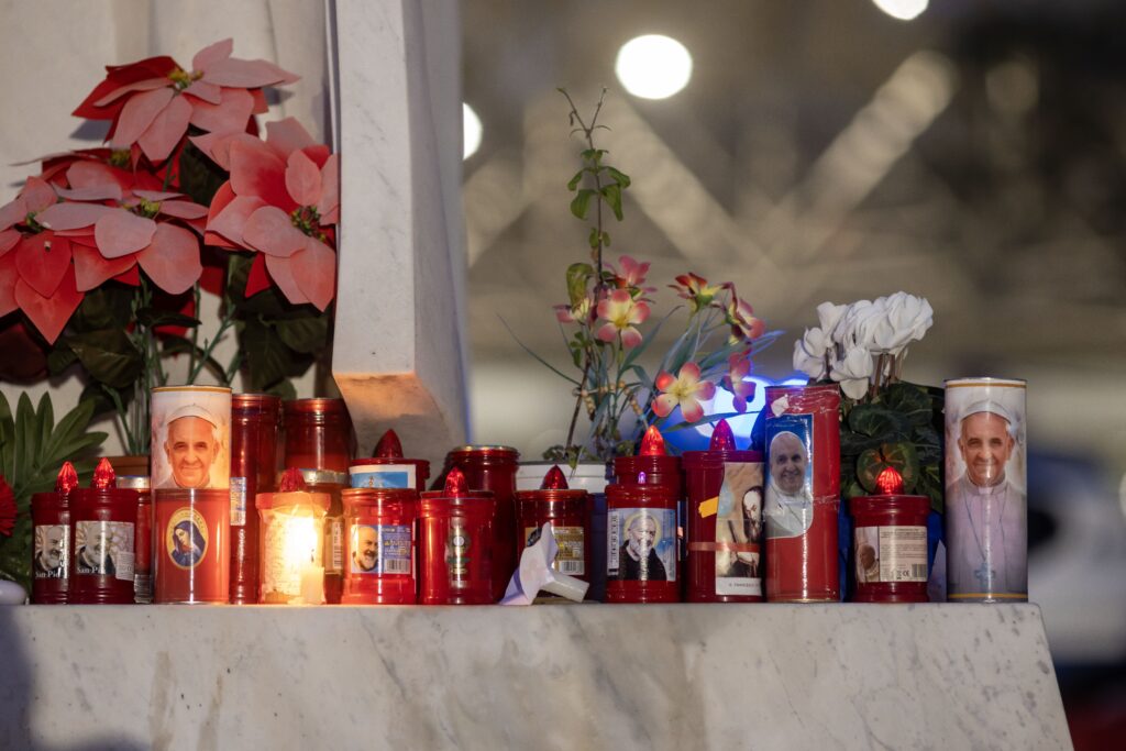 Votive candles and flowers are seen at the base of a statue of St. John Paul II outside Rome's Gemelli hospital on February 19, 2025, where Pope Francis is being treated for double pneumonia.