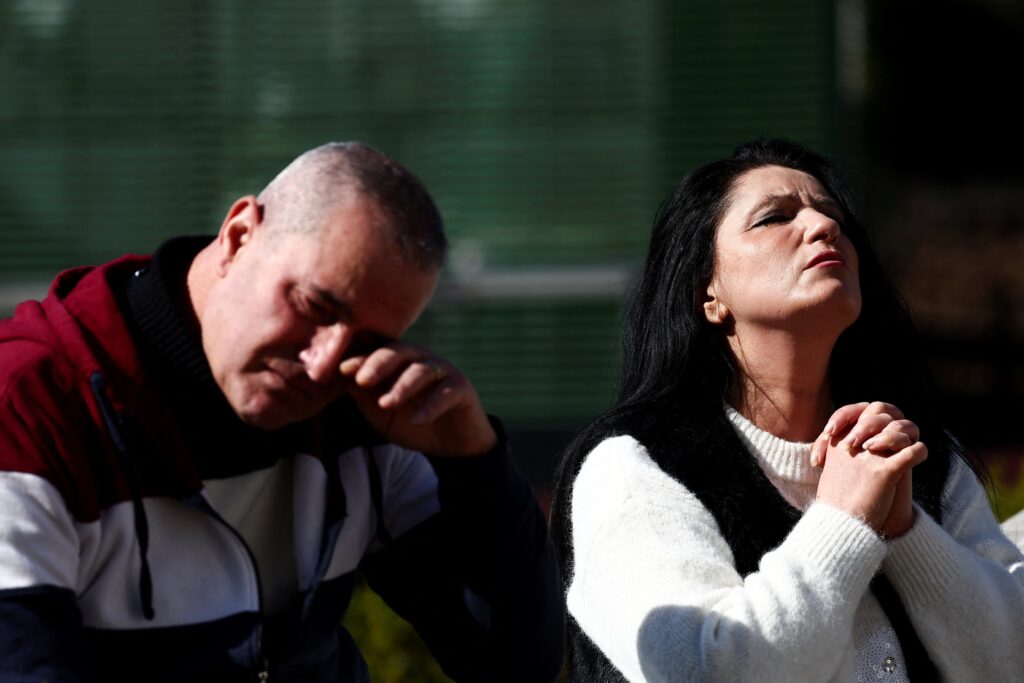 A woman prays as a man reacts next to the statue of St. John Paul II outside Rome's Gemelli Hospital February 20, 2025, where Pope Francis is admitted for treatment for a respiratory infection.