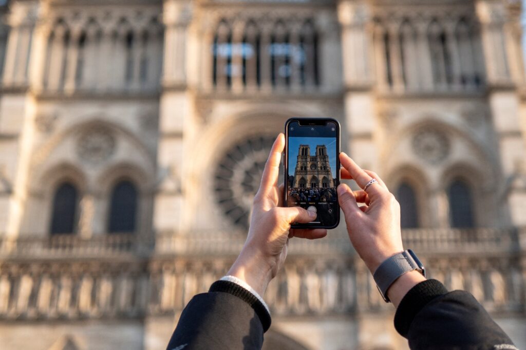 A woman takes a picture with her smartphone in Paris as people line up December 27, 2024, to visit Notre Dame Cathedral, which reopened December 7 after its extensive restoration following a devastating fire April 15, 2019. A mere three months after the reopening, the iconic Gothic cathedral is receiving 29,000 visitors a day, up from 23,500 a day before the fire. (OSV News photo/Gonzalo Fuentes, Reuters)