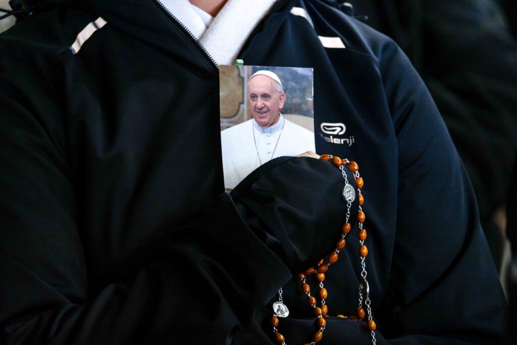 A person holds a rosary and a photo of Pope Francis as people gather in St. Peter’s Square at the Vatican to recite the rosary for Pope Francis with Cardinal Robert F. Prevost, prefect of the Dicastery for Bishops, March 3, 2025. (CNS photo/Pablo Esparza)