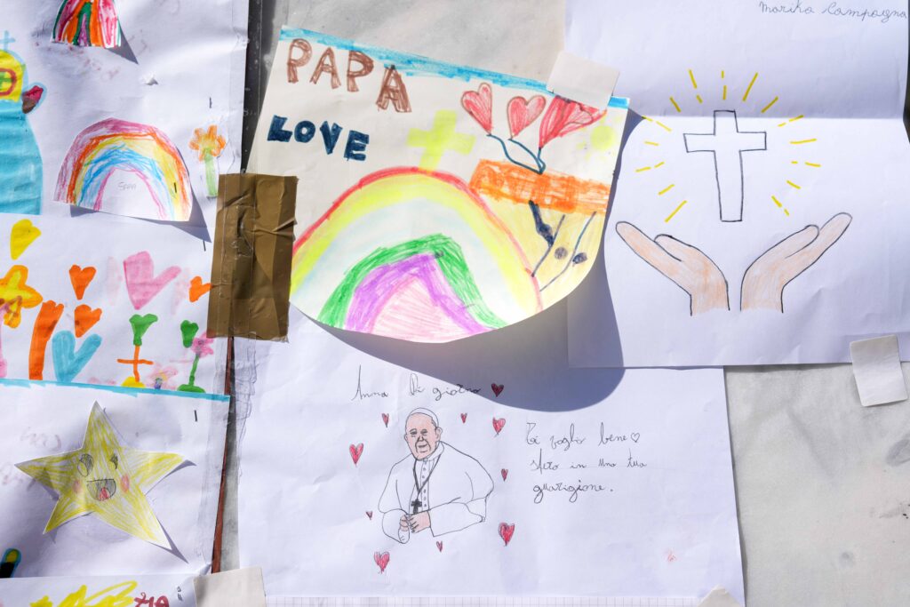 Drawings for Pope Francis are placed at the base of a statue of St. John Paul II outside Rome’s Gemelli hospital March 6, 2025, where the pope has been hospitalized since Feb. 14, receiving treatment for double pneumonia. (CNS photo/Lola Gomez)