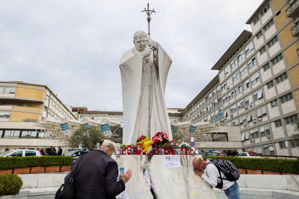 A man and woman pray by the statue of St. John Paul II outside Rome's Gemelli Hospital March 14, 2025, where Pope Francis was admitted February 14.