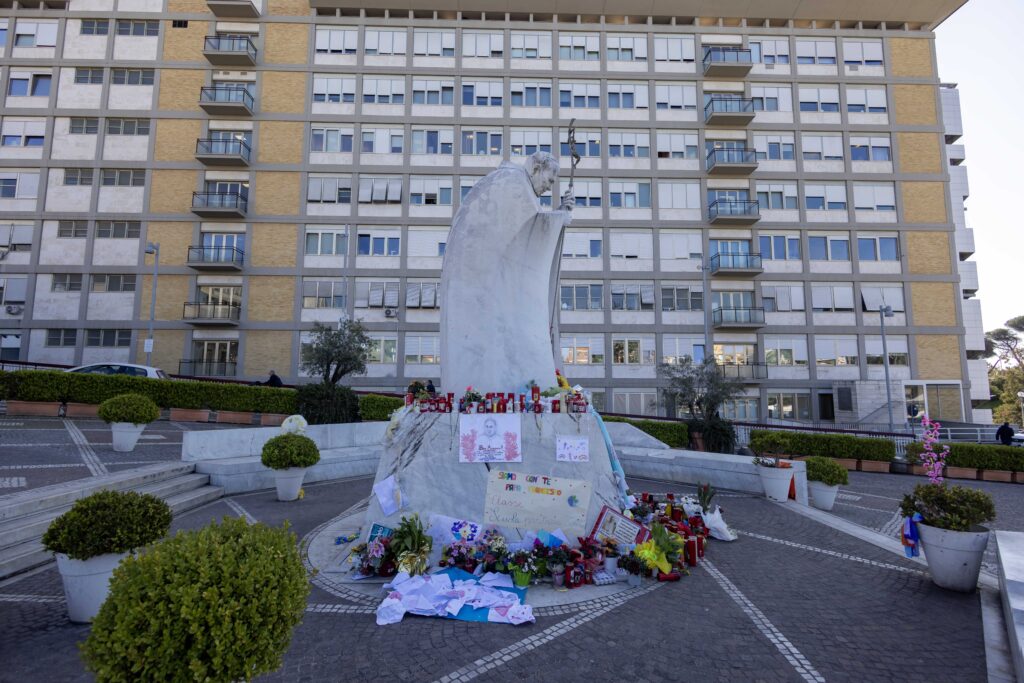 Artículos devocionales, dibujos y mensajes se ven en la base de una estatua de San Juan Pablo II fuera del hospital Gemelli de Roma el 19 de marzo de 2025.