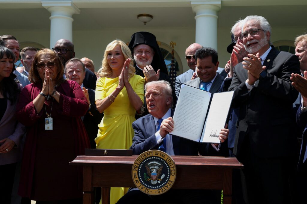 Faith leaders applaud as U.S. President Donald Trump holds up a signed executive order on the "Establishment of the Religious Liberty Commission" during the National Day of Prayer in the Rose Garden at the White House in Washington May 1, 2025. Also pictured in yellow is Paula White, senior adviser to the White House Faith Office. Photo: OSV News photo/Evelyn Hockstein, Reuters
