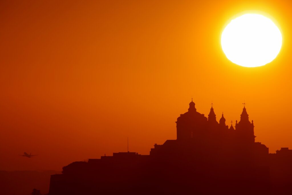 The sun rises behind the Metropolitan Cathedral of St. Paul in the medieval fortified city of Mdina as a plane takes off from Malta International Airport, Malta, in this Jan. 2, 2022, file photo.