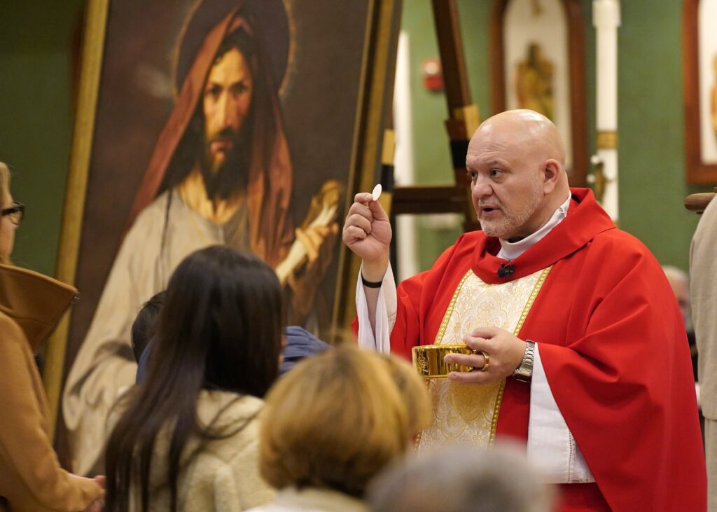 Father Carlos Martins, a member of the Companions of the Cross religious community, distributes Communion during a special Mass celebrated in honor of St. Jude the Apostle at St. Jude Church in Mastic Beach, on November 27, 2023.