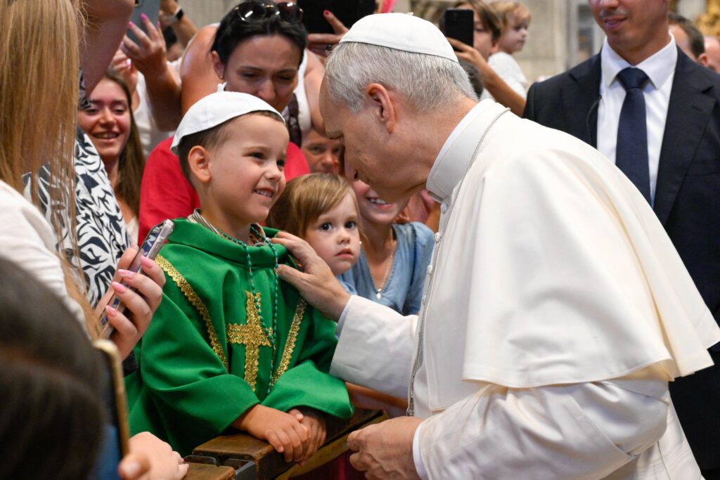 El Papa León XIV saluda a un niño vestido con vestimentas litúrgicas dentro de la basílica de San Pedro en el Vaticano el 20 de agosto de 2025, tras su audiencia general semanal. El Papa visitó a los peregrinos reunidos en la basílica para ofrecerles su bendición, ya que la sala Pablo VI había alcanzado su aforo máximo.