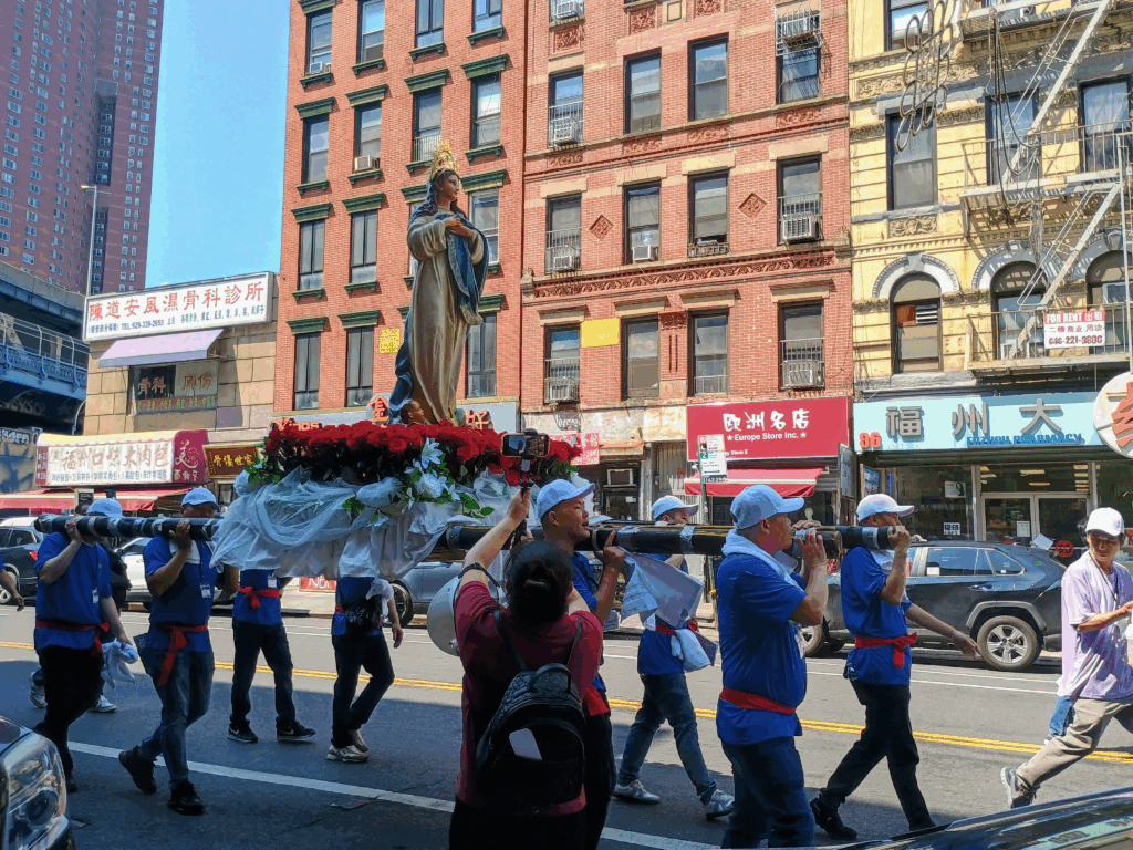 Several men carry the parish statue of the Assumption of Mary on East Broadway during the Assumption Procession organized by the Church of the Transfiguration in Chinatown (Manhattan), Sunday, August 10, 2025.