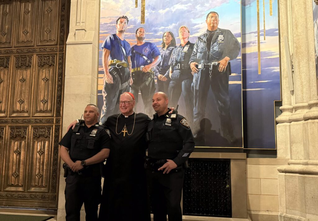 Cardinal Timothy Dolan (center) poses with two New York Police Department officers in front of the first responders panel of St. Patrick’s Cathedral’s new mural, “What’s So Funny About Peace, Love, and Understanding,” unveiled at a press event on Thursday, September 18, 2025.